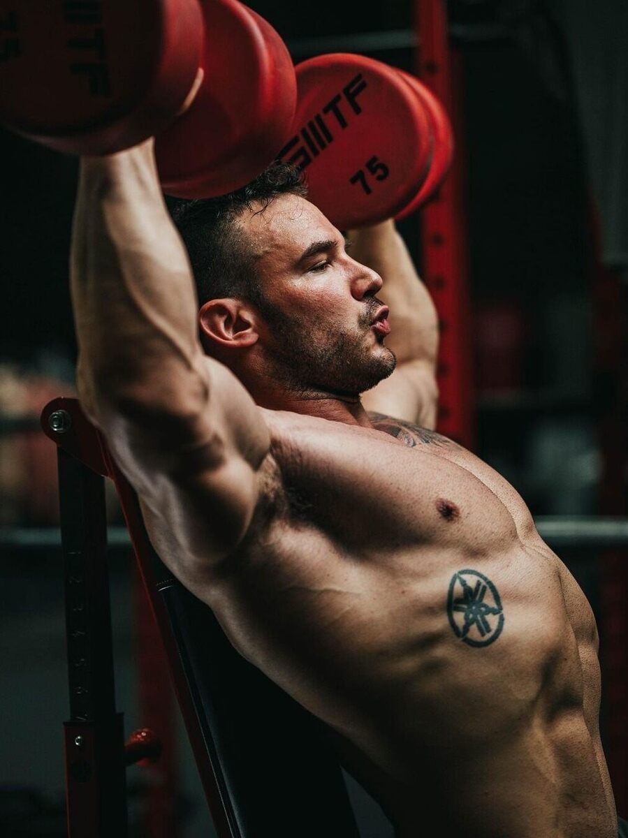 Guy pressing with red dumbbells.